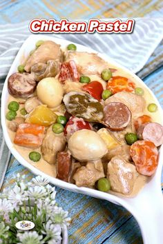 a white bowl filled with meat and vegetables on top of a blue table cloth next to flowers