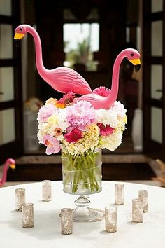 a vase filled with pink flamingos sitting on top of a table next to candles