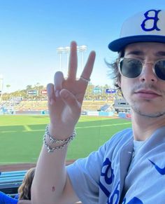 a man with sunglasses and a baseball cap making the peace sign at a baseball game