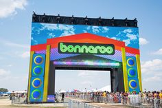 the entrance to an outdoor concert venue with people standing in front and onlookers watching