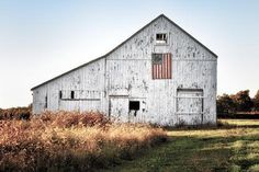 an old barn with the american flag painted on it's side in a field