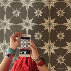 a woman taking a photo with her cell phone in front of a patterned wallpaper