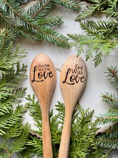 two wooden spoons with the words made with love written on them sitting next to evergreen branches