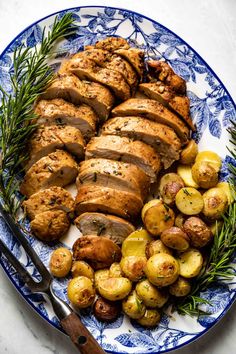 a blue and white plate topped with sliced chicken, potatoes and rosemary sprigs