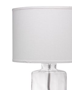 a clear glass table lamp with a white shade on the top and bottom part of it