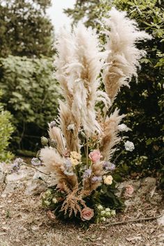 an arrangement of flowers and plants in a vase on the ground near some shrubbery