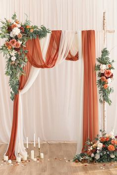 an orange and white wedding arch decorated with flowers, greenery and candles on the floor