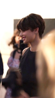 a close up of a person wearing a black dress and smiling at someone in the background