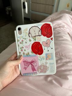 a person holding an iphone case with stickers on it in front of a bed