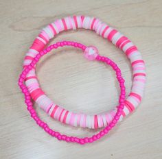 two pink and white bracelets sitting on top of a wooden table