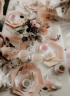 the table is set with pink and white plates, napkins, cups, and flowers