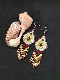 a pair of beaded earrings next to a seashell on a black cloth background