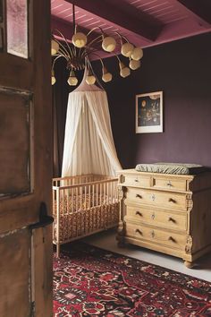 a crib and dresser in a room with purple walls