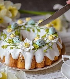 a cake with white icing and flowers on it is being cut by a knife