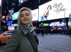 a woman standing in the middle of a busy city street with billboards behind her