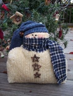 a knitted snowman sitting on top of a wooden deck next to a christmas tree