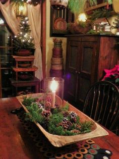 a wooden table topped with a candle surrounded by pine cones and greenery on top of it