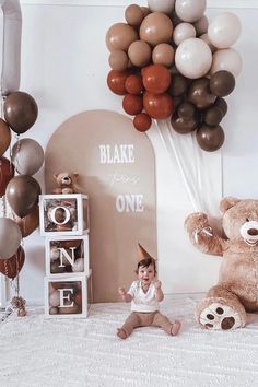 a baby sitting in front of balloons and a teddy bear