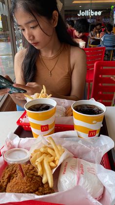 a woman sitting at a table in front of two trays of food with fries and ketchup