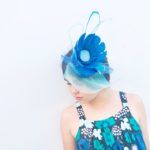 a woman wearing a blue and white hat with feathers on it's head, standing against a wall