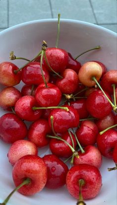 a white bowl filled with lots of cherries on top of a tile floored floor