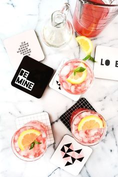 three cocktails on a marble table with cards and coasters next to each other