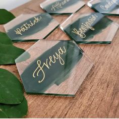 six clear acrylic coasters with gold lettering and green leaves on the table