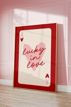 a red and white frame with the words lucky in love on it next to a pink wall