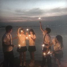 four young people holding sparklers in their hands on the beach at night time,