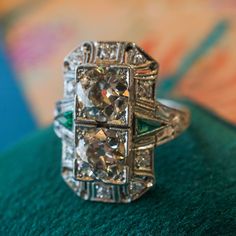 ANTIQUE DOUBLE DIAMOND & EMERALD COCKTAIL RING IN PLATINUM This Antique Double Diamond & Emerald Cocktail Ring in Platinum is what dreams are made of! This one of a kind Art Deco ring features two (2) old European cut diamonds, accent emeralds, and .30 total carats of diamond accents in platinum. With a striking look, the twin old European cut diamonds glitter at the center of a boxy milgrain mounting design. Detailed and utterly attractive, the emerald accents  bring a touch of color the the sp Art Deco Multi-stone Platinum Diamond Ring, Art Deco Multi-stone Diamond Ring, Platinum Emerald Cut Multi-stone Diamond Ring, Vintage Hallmarked Emerald Ring In Platinum, Classic Multi-stone Platinum Diamond Ring, Art Deco White Gold Emerald Ring With Diamond Cut, Art Deco Platinum Multi-stone Rings, Vintage White Gold Emerald Ring With Diamond Cut, Art Deco Multi-stone Platinum Rings