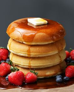 a stack of pancakes with butter and strawberries on the side next to syrup drizzled over them