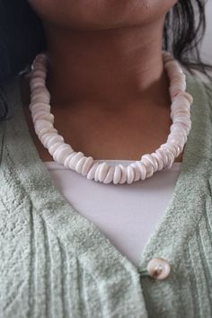 a woman wearing a white necklace with shells on it