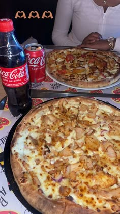 two pizzas sitting on top of metal pans next to soda bottles and cans