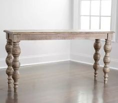 a wooden table sitting in the middle of a room with white walls and wood floors