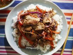 a white plate topped with meat and rice next to chopsticks on a striped table cloth