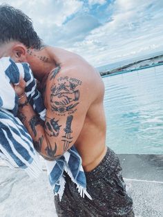 a man with tattoos on his chest and arm wrapped in a towel by the water