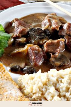 a white plate topped with meat and mushroom stew next to rice on a red table cloth