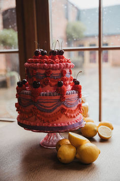 a red cake sitting on top of a table next to lemons and a window