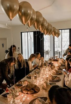 a group of people sitting around a long table with gold balloons hanging from the ceiling