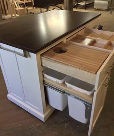 a kitchen island with two trash cans under it and an open drawer in the middle