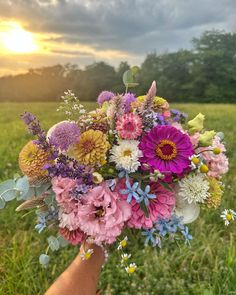 a person holding a bouquet of flowers in their hand on a grassy field at sunset