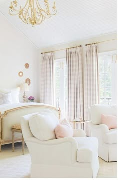 a bedroom with white furniture and chandelier hanging from the ceiling in front of two windows