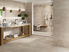 a large bathroom with two sinks and a shower in the corner, surrounded by tiled walls