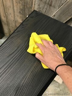 a hand with a yellow cloth on top of a black table next to a wooden bench