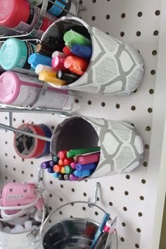 there are two cups with markers and pencils in them on the shelf next to each other