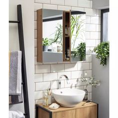 a bathroom sink sitting under a mirror next to a shelf filled with towels and plants