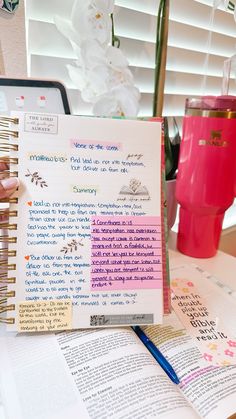 a person holding up a book with writing on it next to a cup and pen