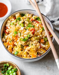 a bowl full of rice and vegetables with chopsticks next to it on a white surface