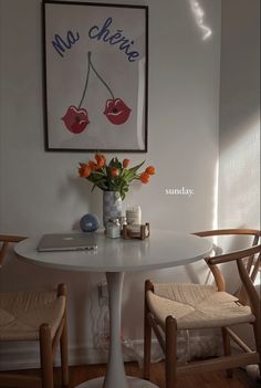 a white table with two chairs and a vase filled with flowers on top of it