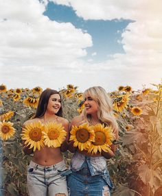 two beautiful young women standing in front of a field of sunflowers holding large yellow flowers